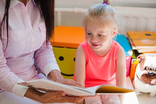 girl in pink shirt reading book with her mom